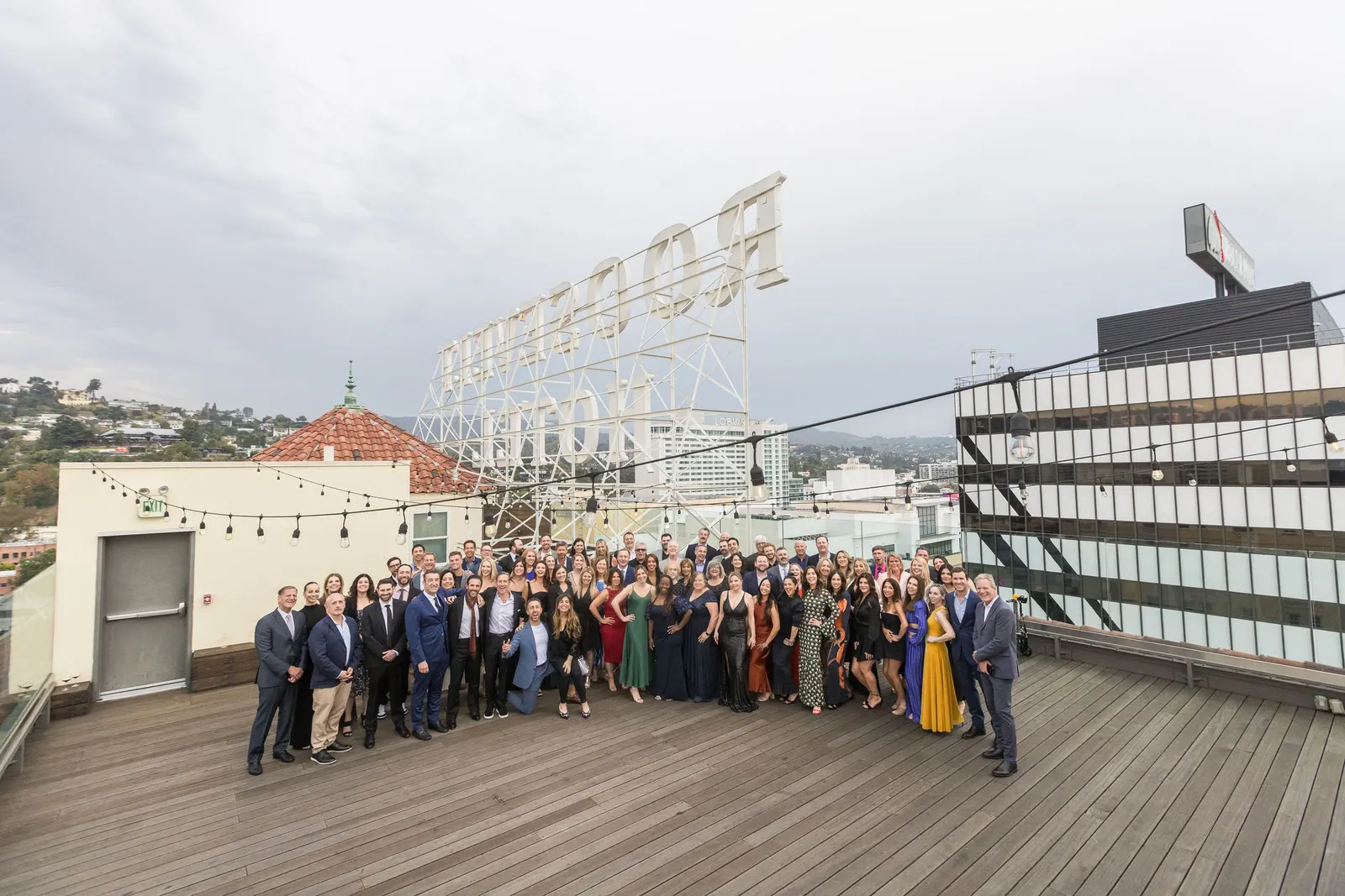 Large group of attendees posing on a rooftop deck at dusk with string lights at the Edge 2025 event, by Marquee Visuals in Los Angeles.