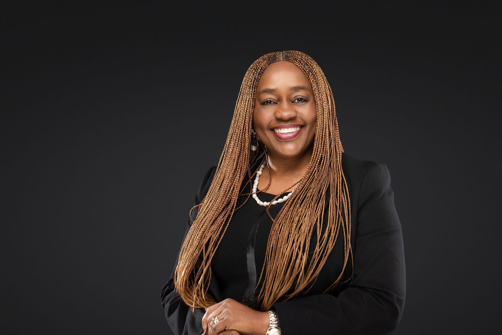 Executive headshot of a woman with long braided hair and a black blazer, arms crossed, on a soft gradient gray backdrop, by Marquee Visuals in Los Angeles.